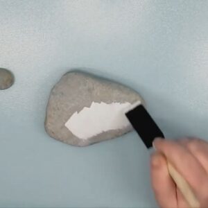 painting a rock white using acrylic paint and a sponge.